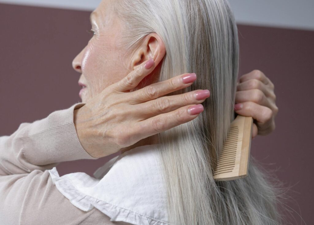Elderly woman with silver hair combing her hair, highlighting graceful aging and care.
