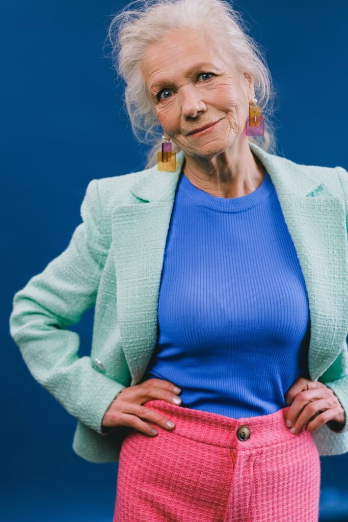 Stylish elder lady with hands on waist looking at camera on blue backdrop