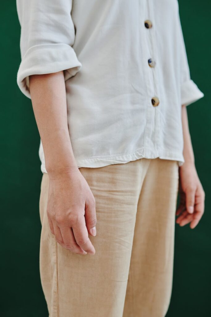 Close-up of a person in a minimalist white shirt and khaki pants against a green backdrop.