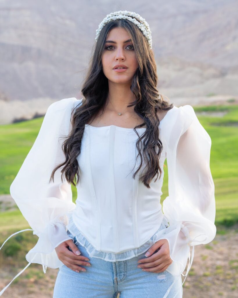 A woman poses confidently outdoors in a sheer white blouse, adding elegance to the natural setting.