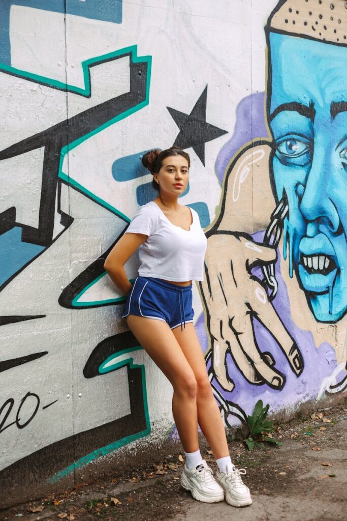 Fashionable young woman in streetwear posing by a colorful graffiti wall outdoors.