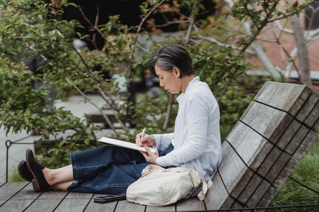 Woman sketching in peaceful outdoor garden, showcasing artistic creativity and relaxation.