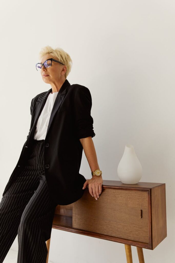 Confident senior businesswoman leaning on table in stylish modern attire with eyeglasses, smiling.