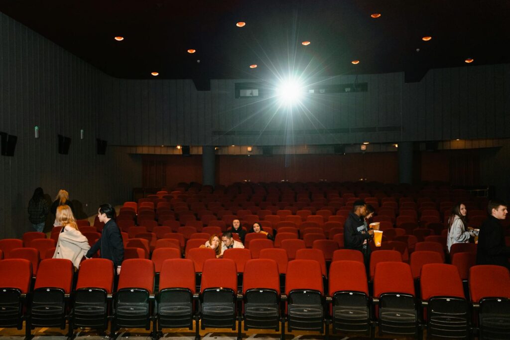 People leaving a dimly lit cinema with red seats after a movie.
