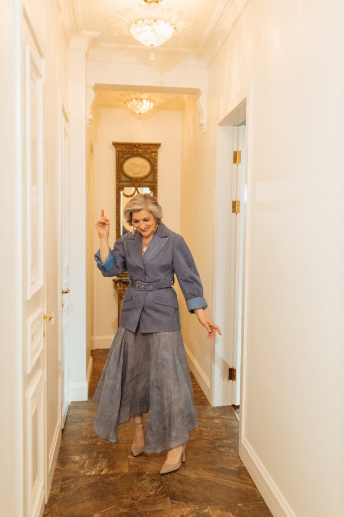 Senior woman in stylish outfit dancing joyfully in a well-lit hallway.