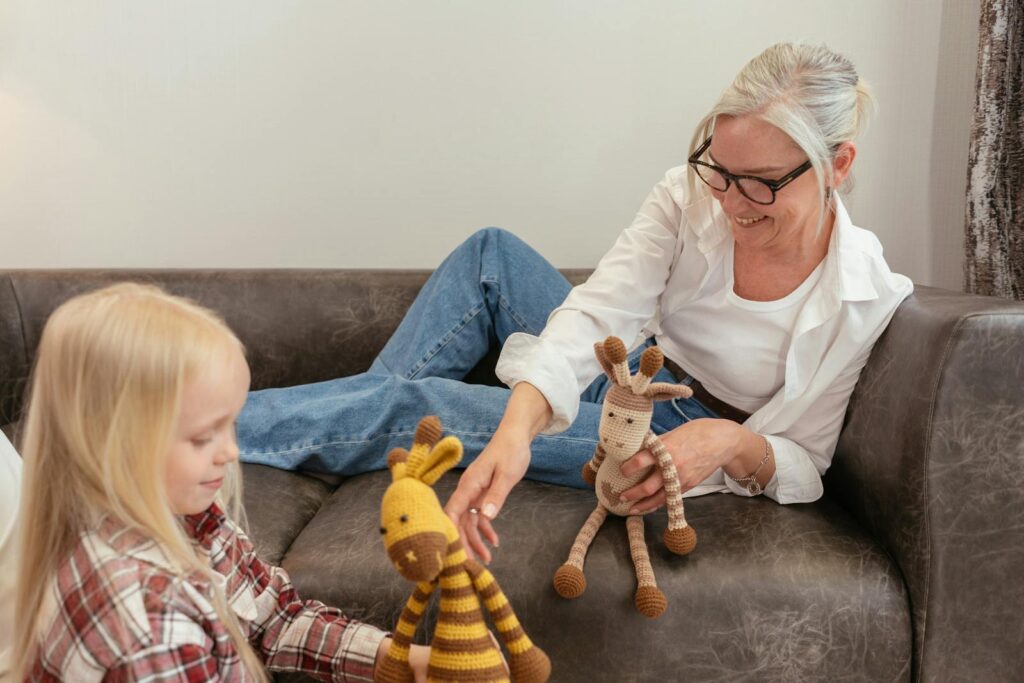 A grandmother and granddaughter having fun with knitted toys on a sofa, showcasing family bonding moments.