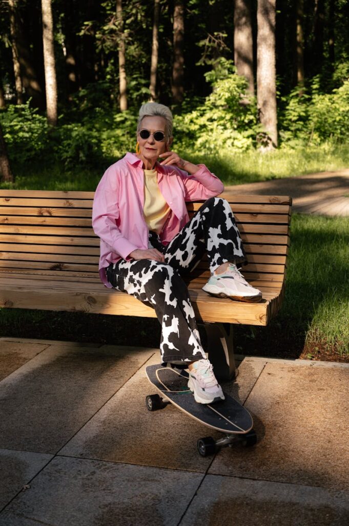 Elderly woman in sunglasses skateboard sitting stylishly in a park on a sunny day.