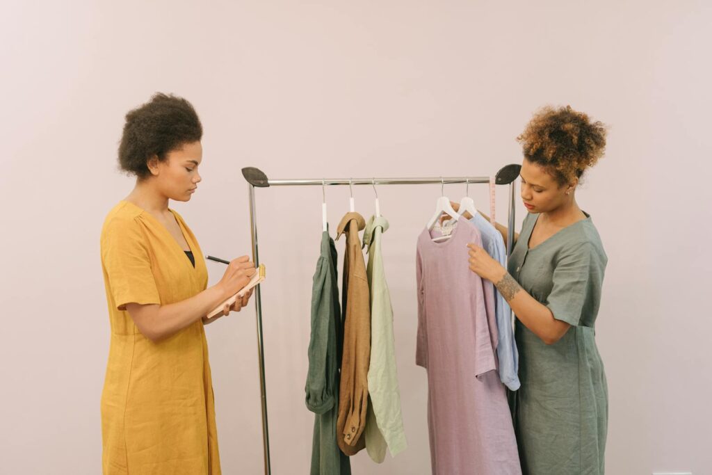 Two women working together in a fashion design setting, reviewing clothing options on a rack.