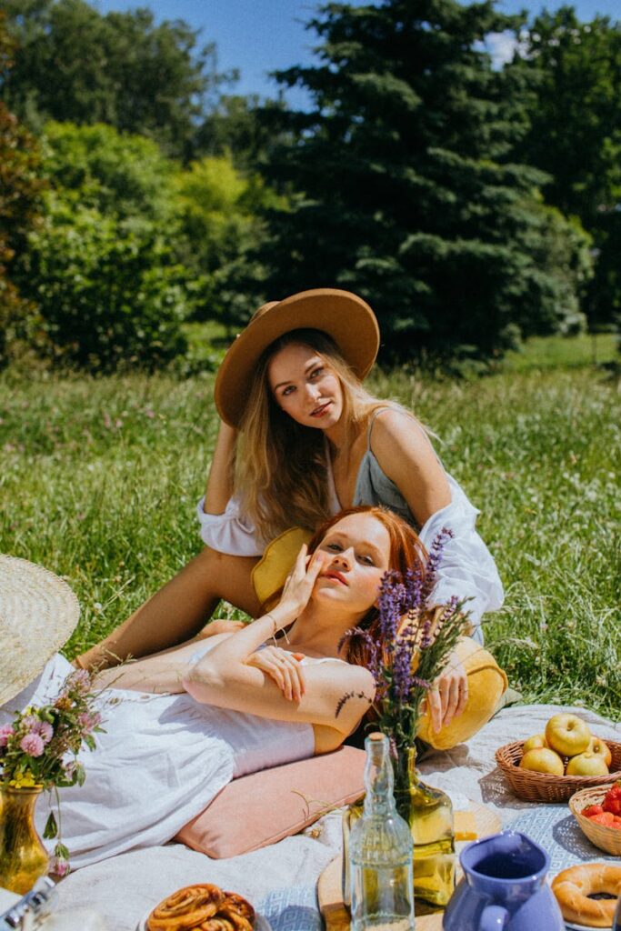 Two women enjoy a sunny picnic outdoors with flowers, fruits, and pastries.