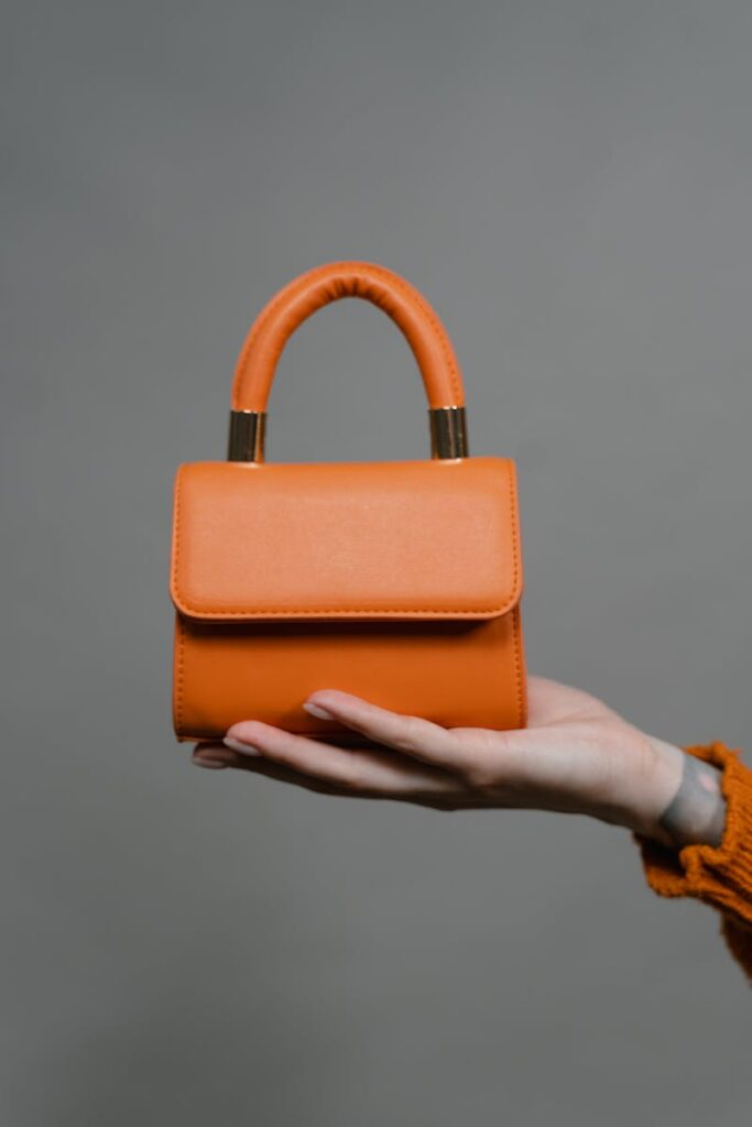 Trendy orange mini handbag showcased with elegant hand, perfect for fashion-forward collections.