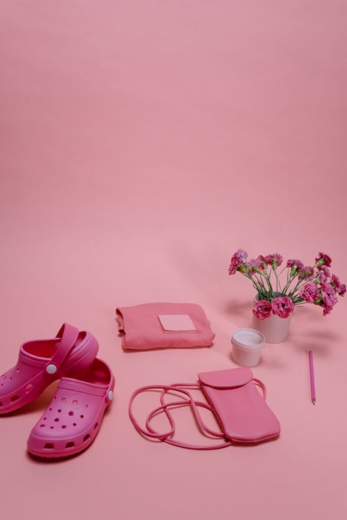 Creative flat lay of pink shoes, bag, and flowers on a pastel background.