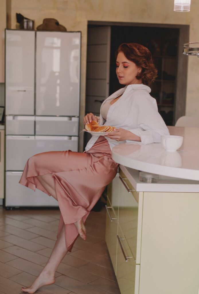 Woman in stylish attire eating breakfast waffles in a modern kitchen setting.