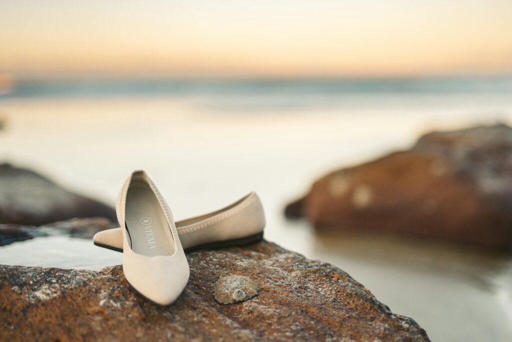 Chic beige flat shoes resting on seaside rocks with a serene sunset backdrop.