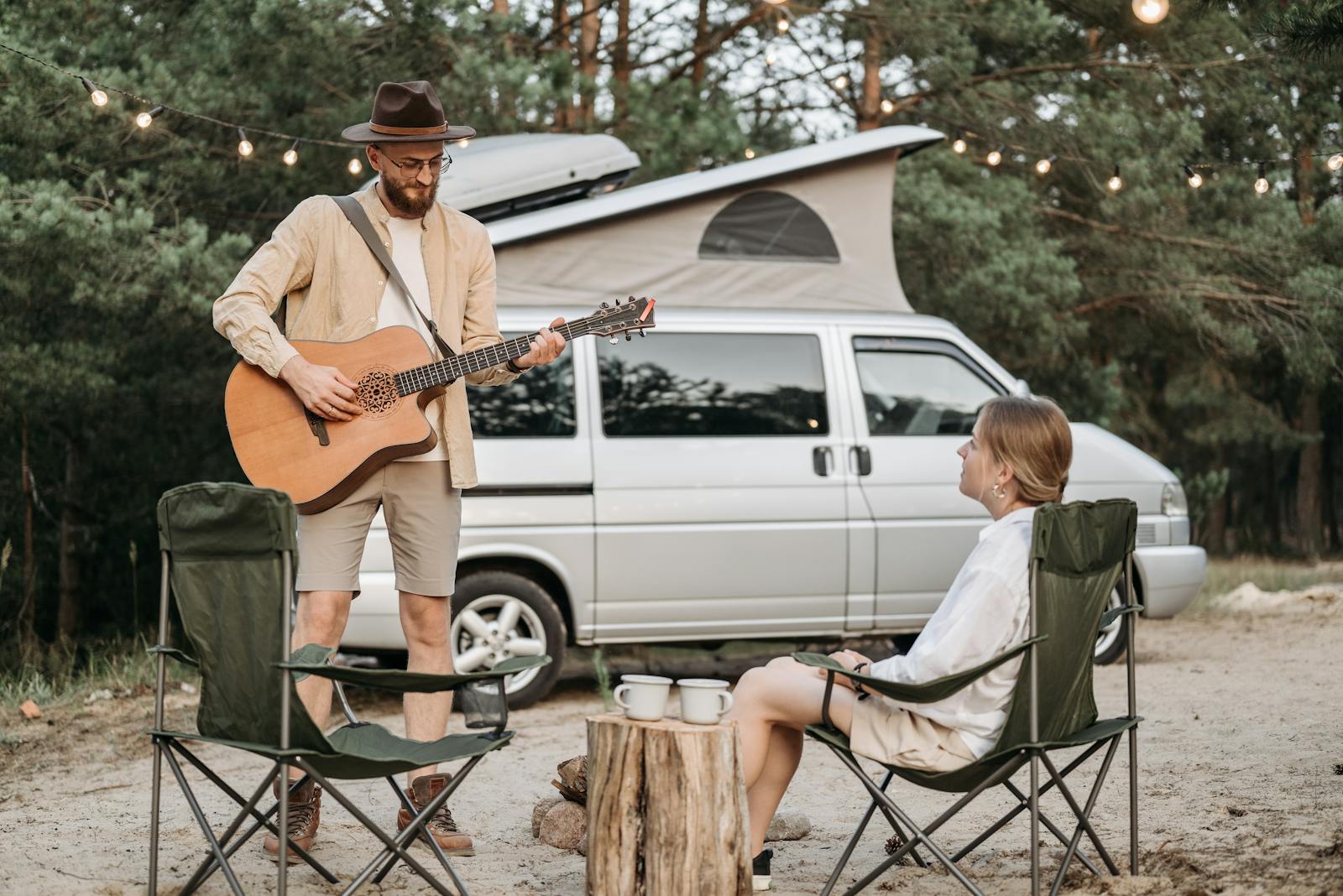 A couple enjoys a romantic outdoor camping experience with guitar music by their campervan.