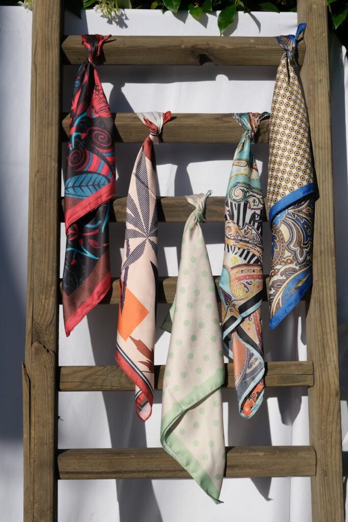 Vibrant scarves with various patterns displayed on a wooden ladder against a sunny backdrop.