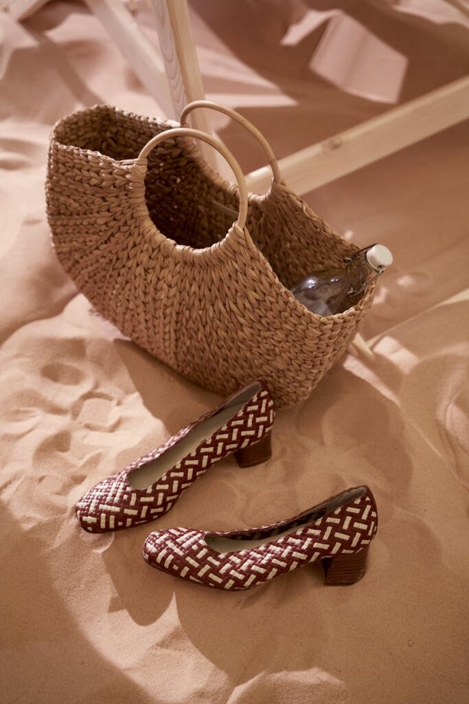 Wicker bag and patterned shoes on sand, embodying summer style.