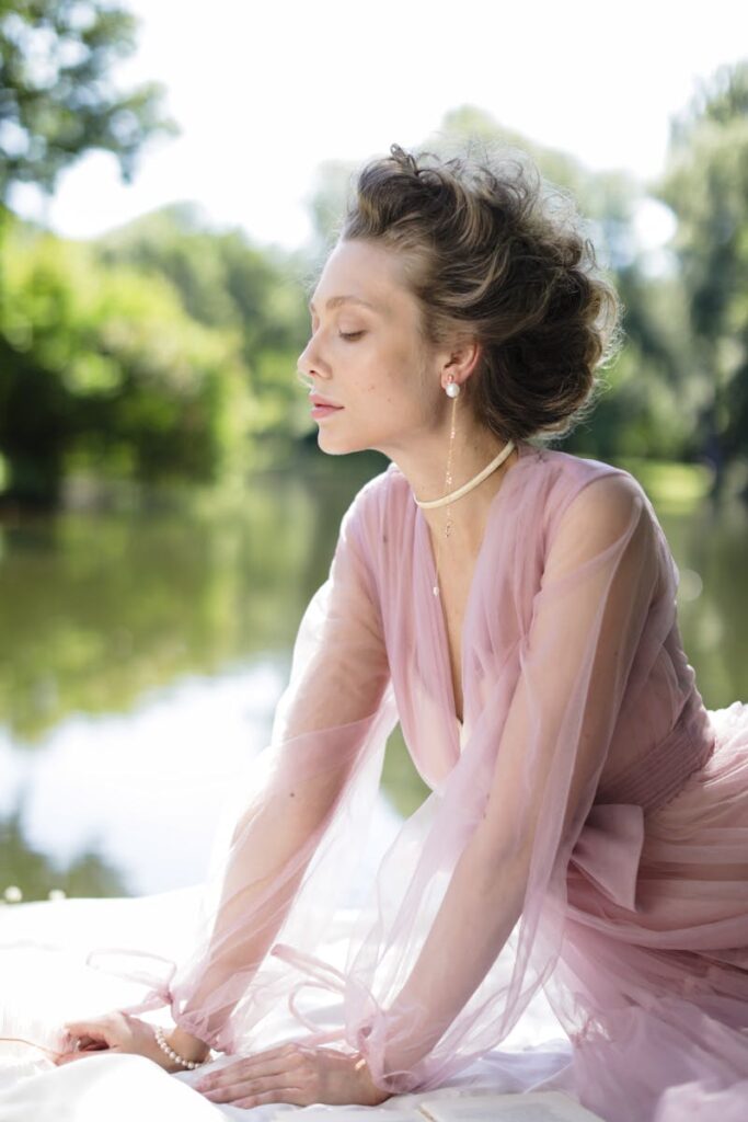 A serene woman in a pink dress enjoys tranquility by the water. Perfect for lifestyle themes.