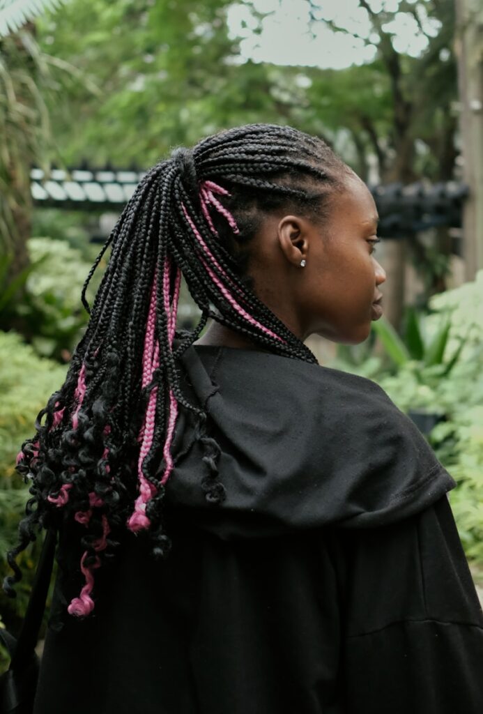 a woman with pink and black dreadlocks standing in a garden