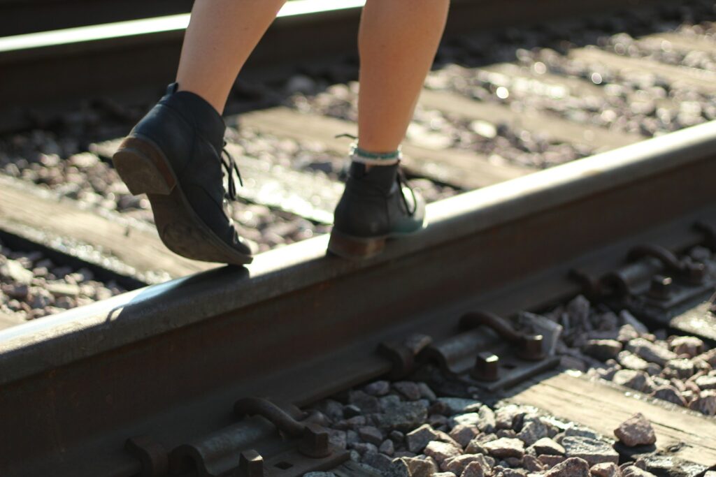 person in black and white nike sneakers standing on train rail during daytime