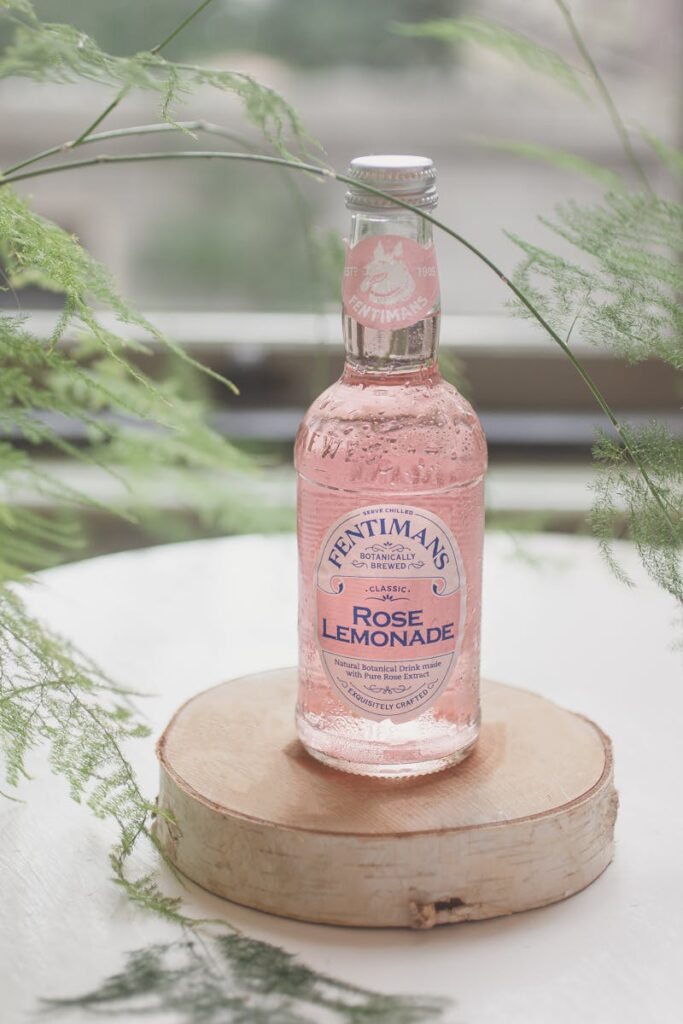 Close-up of a Fentimans Rose Lemonade bottle on a wooden coaster with greenery.