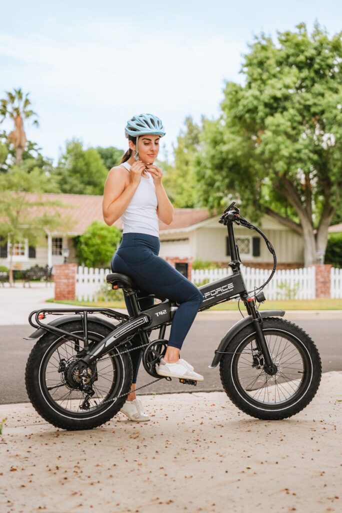 Caucasian woman with helmet adjusting straps while sitting on a bicycle in a suburban neighborhood.
