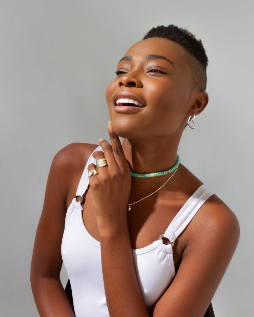 Elegant portrait of a fashionable woman with short hair and jewelry posing against a white background.