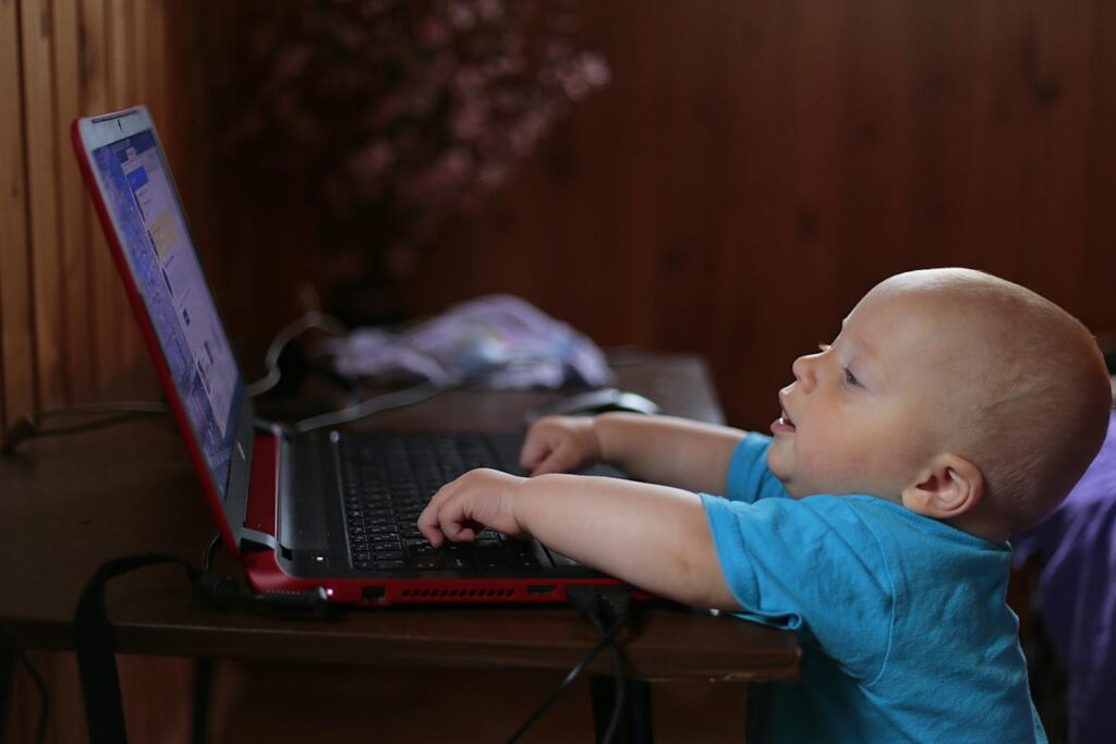 Cute baby boy engaged with a laptop indoors, showing early tech curiosity.
