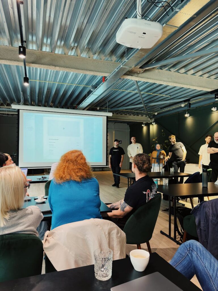 A group of people attending a presentation in an industrial-style office in Amsterdam.
