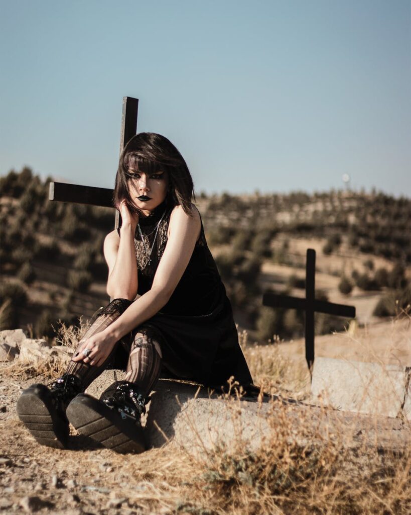 Emotive scene of a gothic woman sitting near crosses in a rural setting.