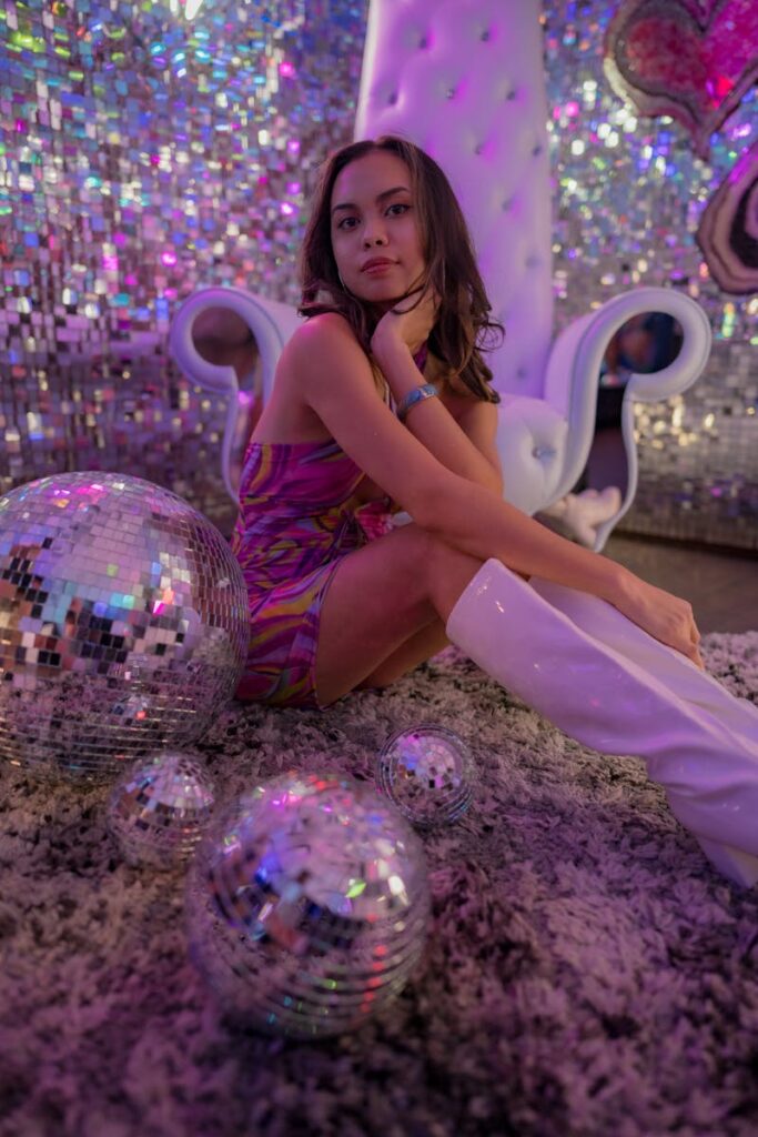 Stylish woman poses with disco balls in a vibrant, sparkling indoor setting, exuding retro glamour.