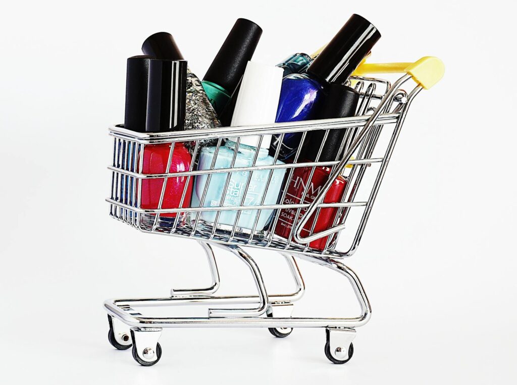 Colorful nail polish bottles in a mini shopping cart against white background.