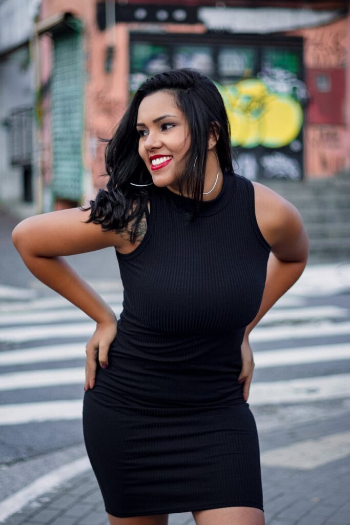 Confident woman in black dress smiling in a vibrant urban street.