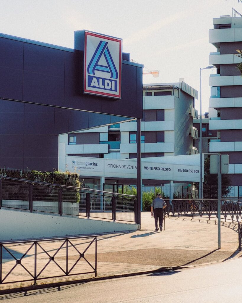 A city landscape featuring an ALDI store and nearby apartment buildings on a sunny day.