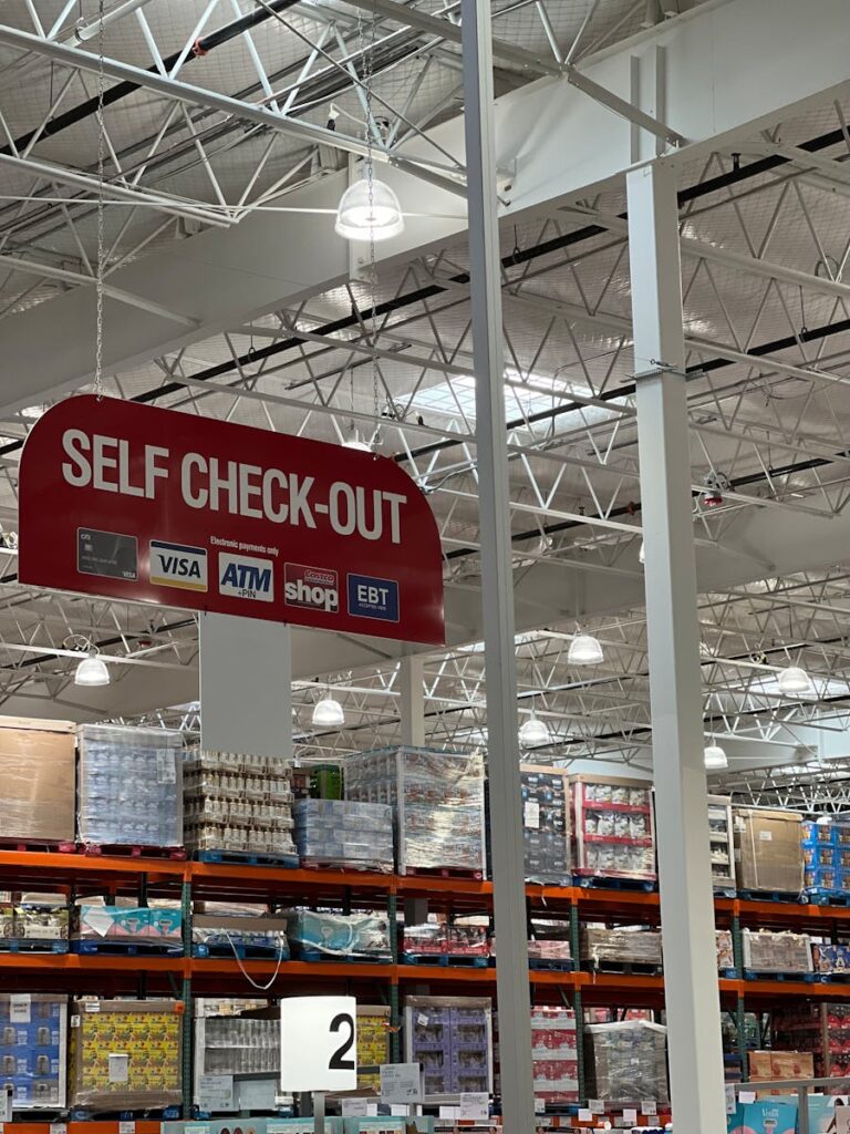 Self check-out section in a large warehouse store with visible payment options.