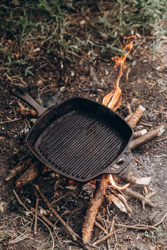 A cast iron grill pan heating over an open campfire, ideal for outdoor cooking.
