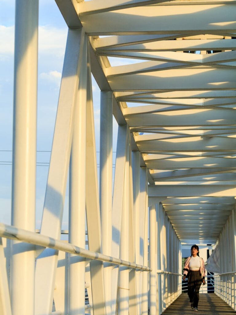 A woman walks along a modern white footbridge in the soft morning light, showcasing architectural patterns.