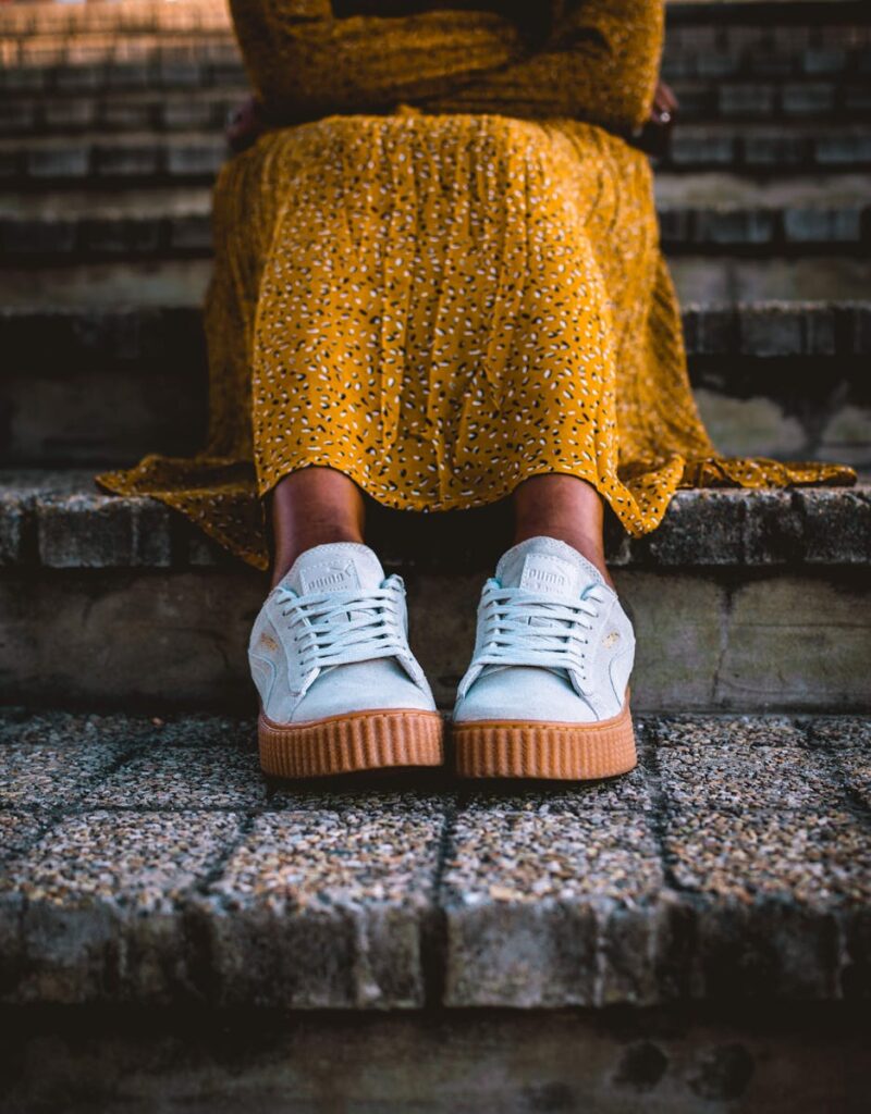 A close-up shot of a woman in a yellow dress and white sneakers sitting on stone steps.