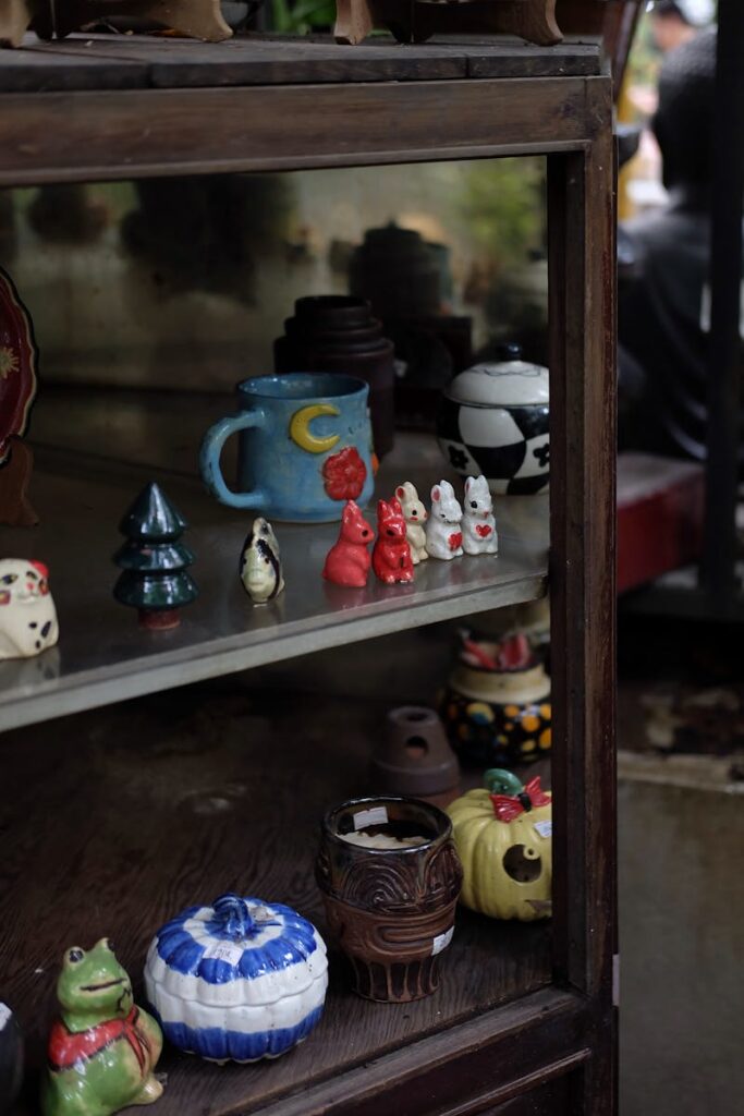 A wooden shelf displaying various colorful ceramic figurines and mugs in an outdoor setting.