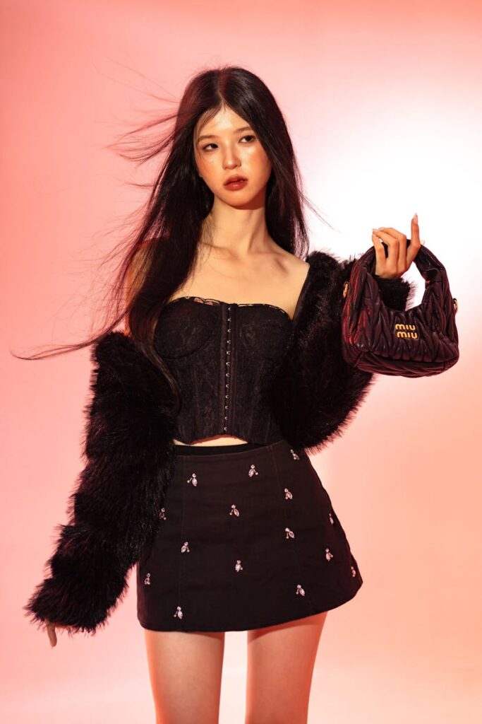 Trendy young adult posing with stylish apparel and handbag against pink background.