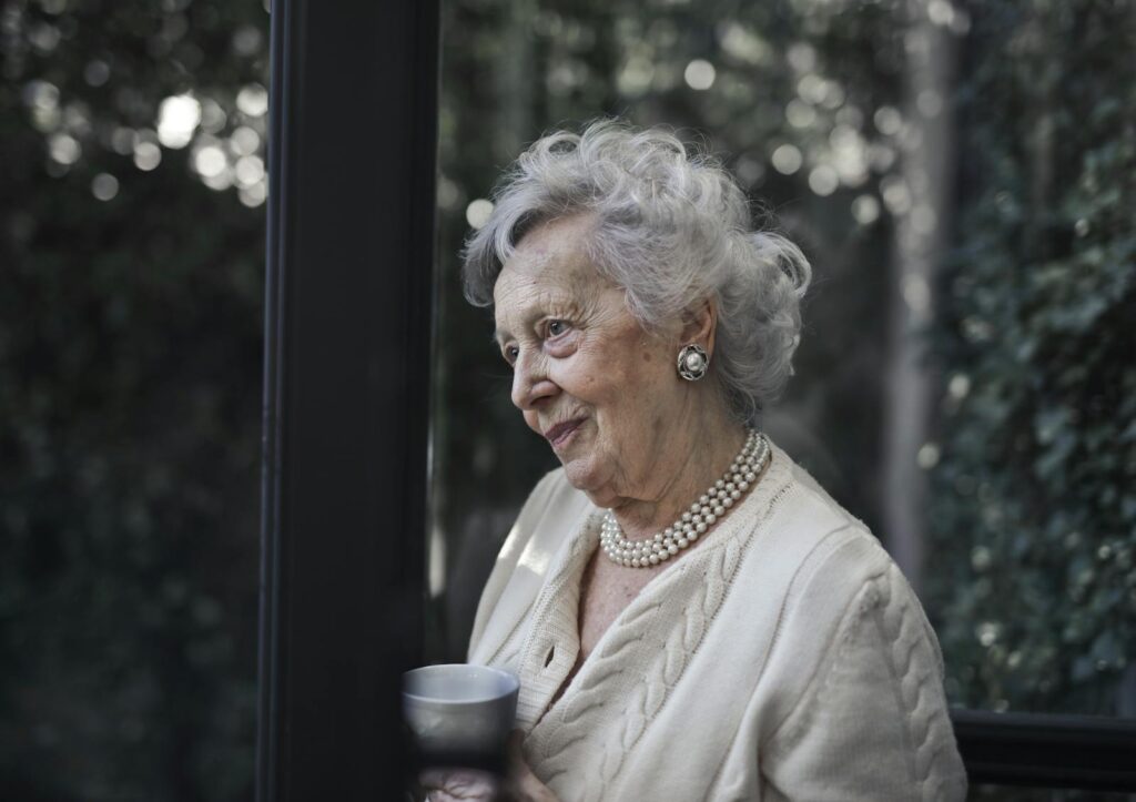Senior woman with white hair and pearls enjoying a quiet moment indoors.