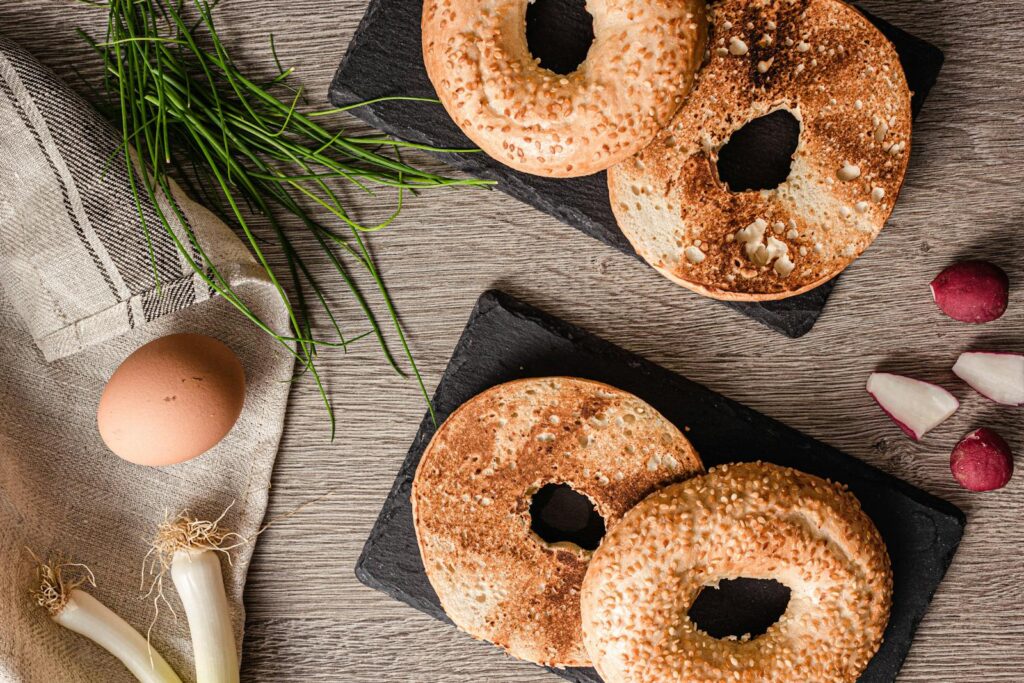 Top view of toasted bagels with fresh scallions, egg, and radishes on a wooden table.