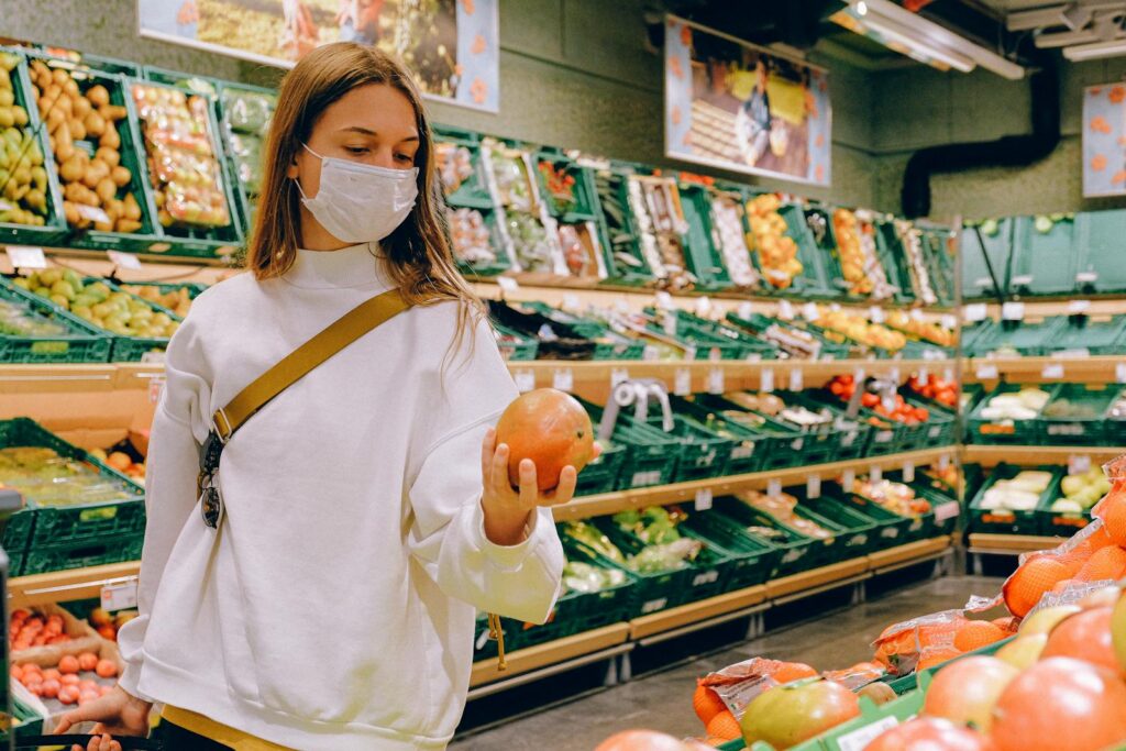 Woman wearing a face mask choosing fruits in a supermarket for safe shopping during pandemic.