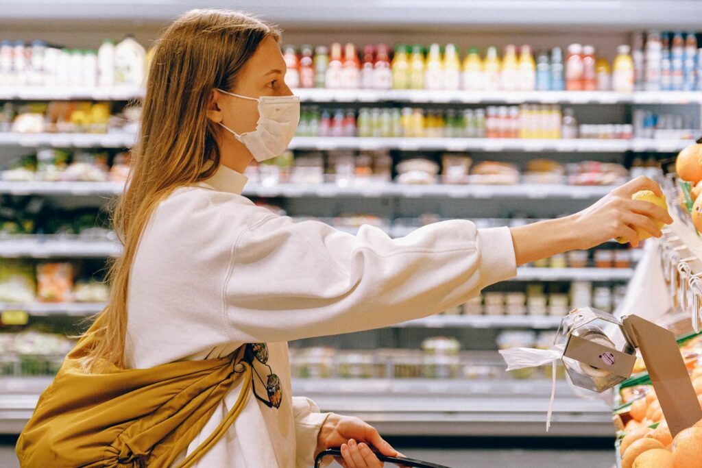 Woman wearing a face mask while selecting fruit in a supermarket, highlighting safety measures.