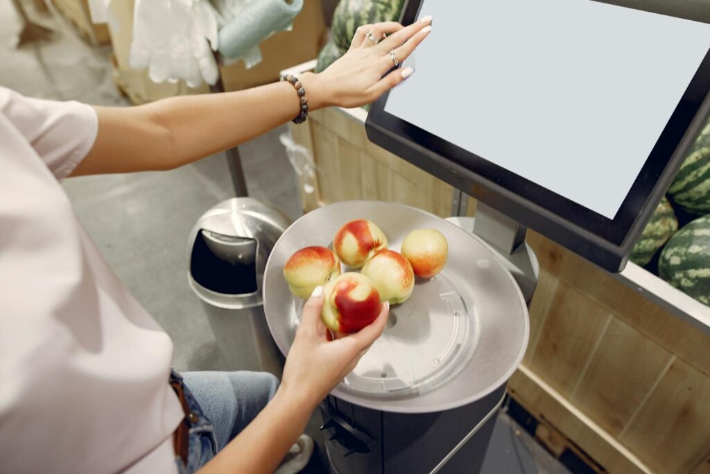 From above of unrecognizable woman touching screen of electronic scales and putting peaches while weighing peaches on scales in contemporary supermarket