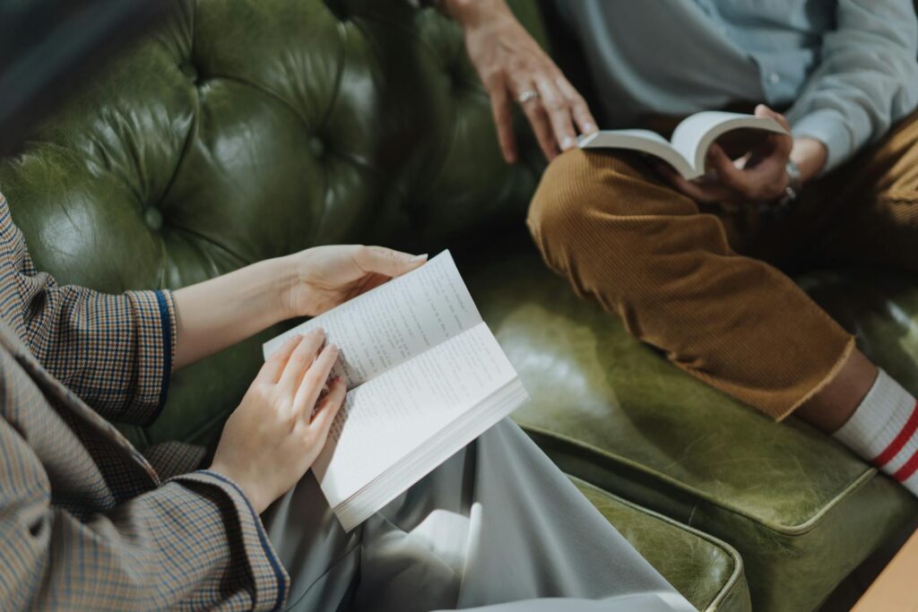 Two adults sitting on a sofa, engaged in reading books, creating a peaceful atmosphere.