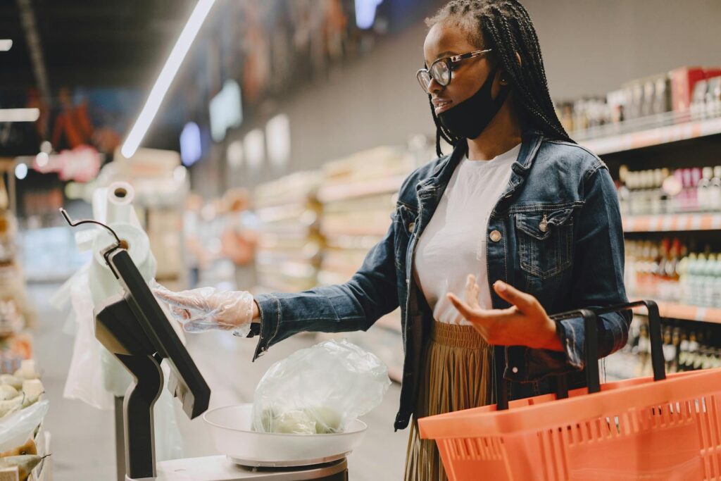 A woman weighing vegetables in a supermarket using a digital scale with a shopping basket.