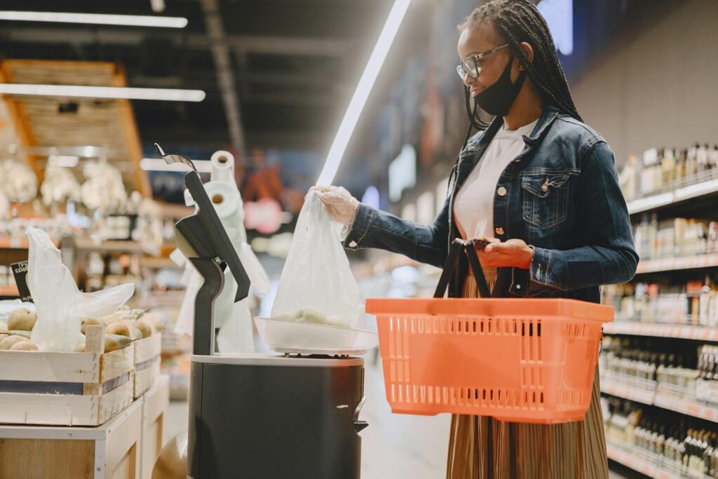 Young woman wearing a mask shops in a modern grocery store with a basket and fresh produce.