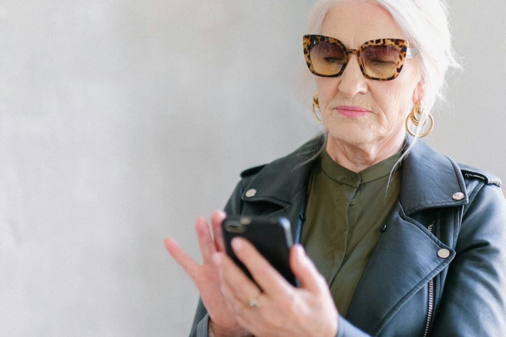 Senior woman in stylish outfit using a smartphone indoors, embodying elegance and tech-savvy living.