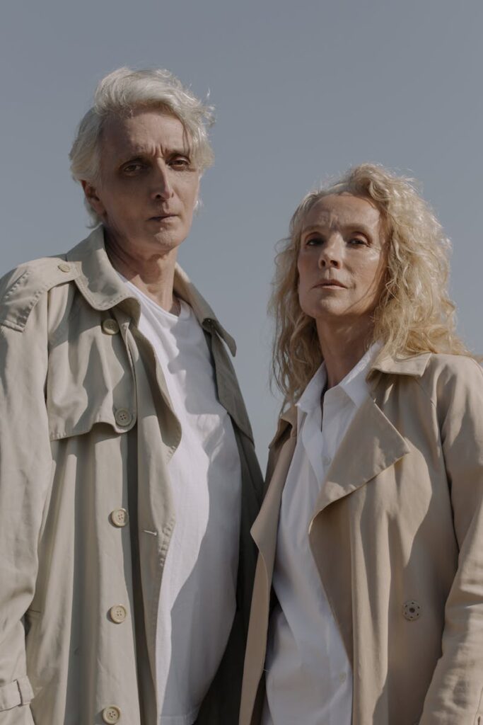 Elegant senior couple standing outdoors, exuding style and romance in matching trench coats.