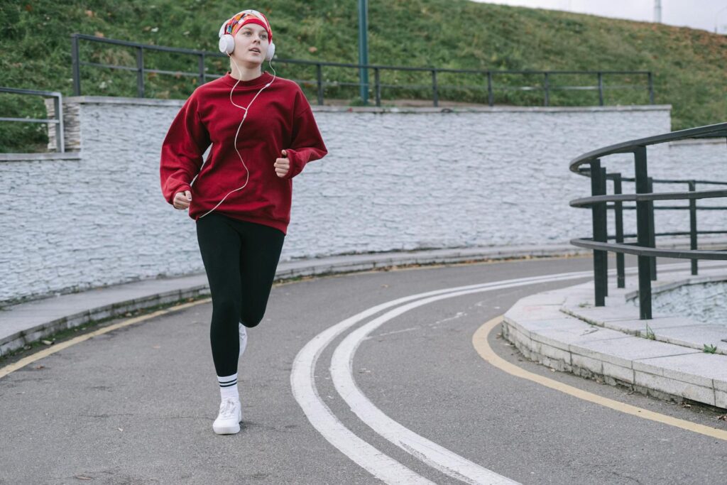 Female jogger in red sweatshirt exercising outdoors, wearing headphones.